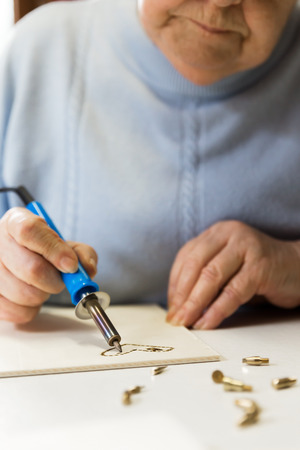 senior adult woman is doing woodburning as art therapy, verticalの写真素材