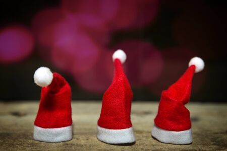 three christmas hats on a wooden table, red and purple blurs in the backgroundの写真素材