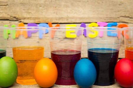 colorful easter eggs and cups of dye in front of a wooden backgroundの写真素材