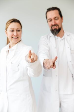 two medic professionals are standing, both are pointing with their fingers to the viewer, concept touchscreenの写真素材