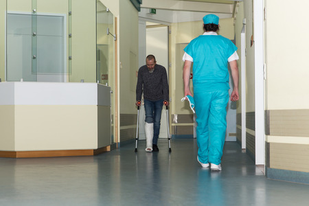 male patient with cast and surgeon walking on hospital corridorの写真素材
