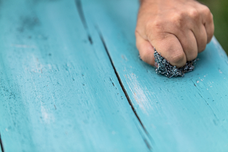 wooden planks with chalky paint is getting sanded with steel wool for old looking finishの写真素材