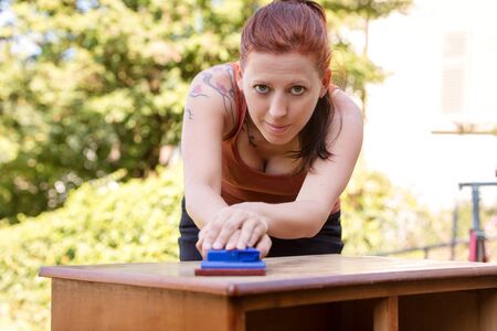 pretty woman is sanding a dresser by hand, preparing for paintingの写真素材