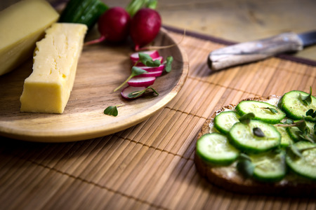 slice of bread with cucumber and cress, wooden plate with cheese and radishesの写真素材