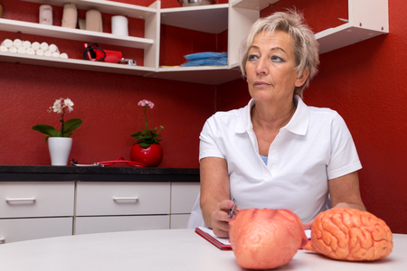 female internist thinks about something in her office, plastic heart and brain on a tableの写真素材