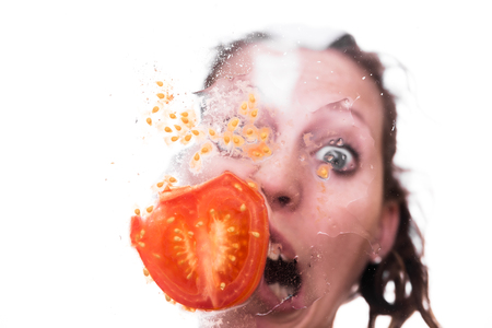 funny female face making a grimace, with tomato behind a pane, studio shotの写真素材