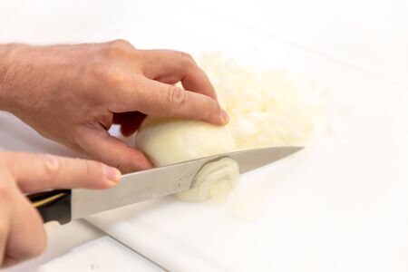 Man is cutting a raw white onion with a knife in slices and cubes, copy spaceの写真素材