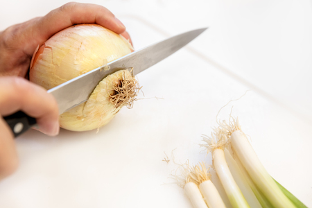 Man is cutting a fresh onion and escallion on white chopping boardの写真素材