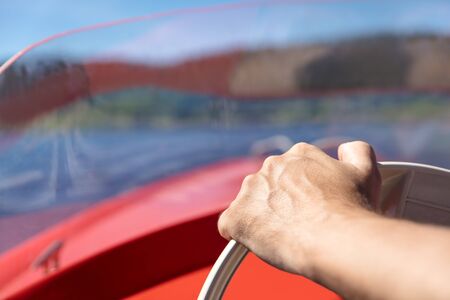 Close up from a male hand on a wheel of a motorboat, blue lake backgroundの写真素材