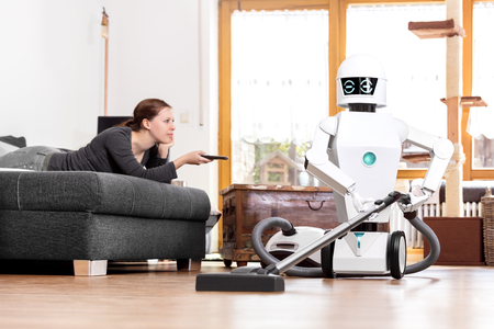 woman is enjoying her leisure while a robot is doing the work in the household. aai is vacuuming the floorの写真素材