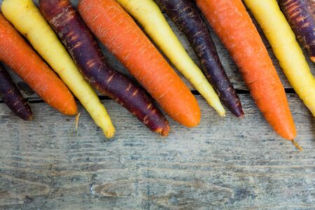 various carrots in the colours purple, orange and yellow on a table, laying in a row