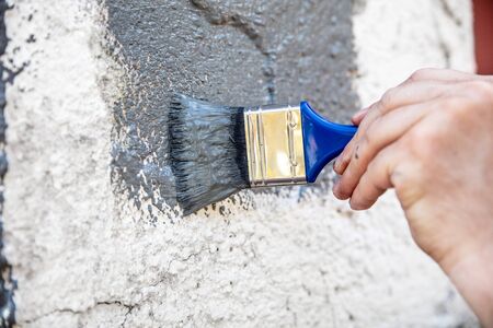 Man is painting and renewing a stone wall with grey paint, hand and brush in the frontの写真素材