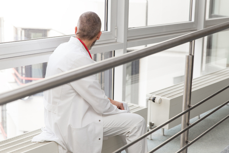 doctor or surgeon is sitting thinkful at a window looking through, having a breakの写真素材