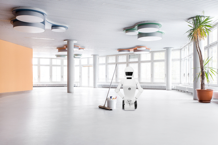 cleaning service roboter in the middle of a big hall, is doing his cleaning work with a broomの写真素材