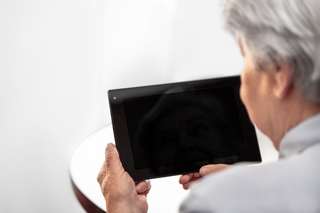 Backview of a elderly woman is holding a tablet with copyspace, concept learning and technology
