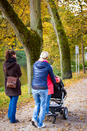 two women and girl walking with a buggy through the park