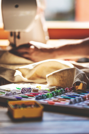 lot of sewing equipment on a wooden table, sewing machine in the background