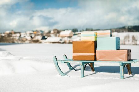 Vintage wooden slegde with presents standing in the snow, rural village in the backgroundの写真素材