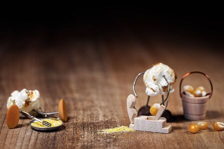 funny popcorn figure is grinding or slicing a raw corn to produce polenta or cornmeal or flour, wooden table and black backgroundの写真素材