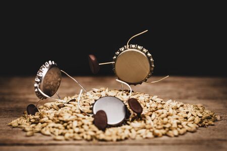 Crown cork miniature figures on malted barley, humorous conceptual scene with ingredients for brewing beerの写真素材