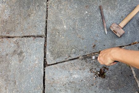 man is cleaning the mortar joints of a flagstone floor with stone mason tools, like hammer and...