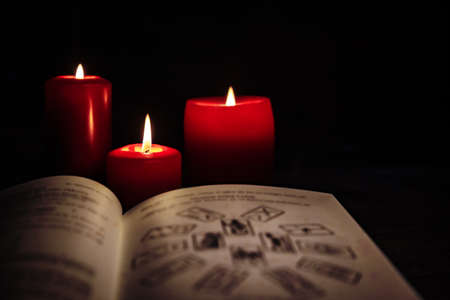 Old book with tarot cards and red candles in front of black background, horoscope and fortuneteller, copyspaceの写真素材