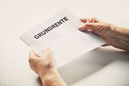 Senior or pensioner holding a letter with german word grundrente, basic pension, copyspaceの写真素材