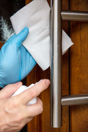 Man disinfecting the front door in days of the corona pandemic, hygienic and protection, details