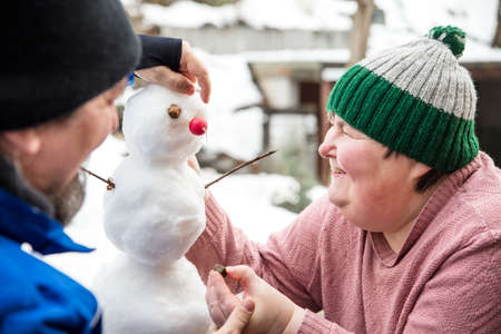 a mentally handicapped or disabled woman and a man forms a snowman outdoors, having fun togetherの写真素材