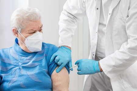 a doctor or nurse gives a senior a shot, perhaps a vaccination. The old woman wears a ffp2 maskの写真素材