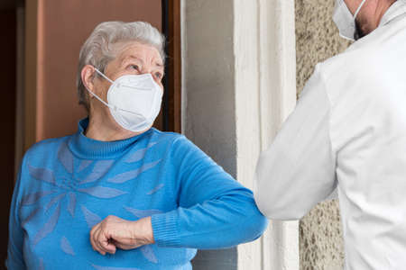 a senior citizen and a doctor or nurse greet each other with their elbowsの写真素材