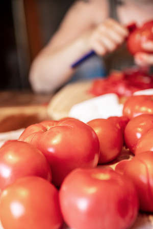 a woman is peeling a lot of red fresh and boiled tomatos with a knife, preparing for cooking a sauceの写真素材