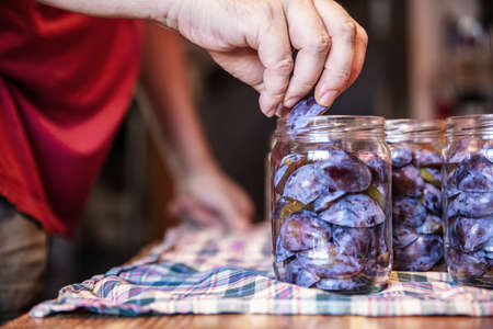 a man is filling glasses with plums, preparing for preserving the fruits, concept self supporter or...