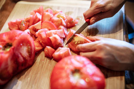 a woman is peeling a lot of red fresh and boiled tomatos with a knife, preparing for cooking a sauceの写真素材