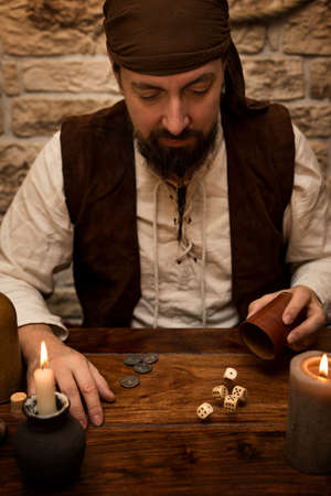 a medieval man sitting on a table and playing dice, concept gamblingの写真素材