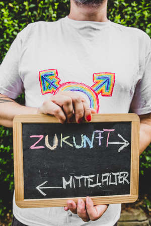 man with painted fingernails holds a sign with german text, concept lgbt and diversity. text means future and medievalの写真素材