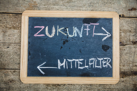 blackboard with german text which means future and middle ages, wooden table as background, concepts...
