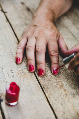 a man paints his fingernails with red nail polish, wooden table as backgroundの写真素材