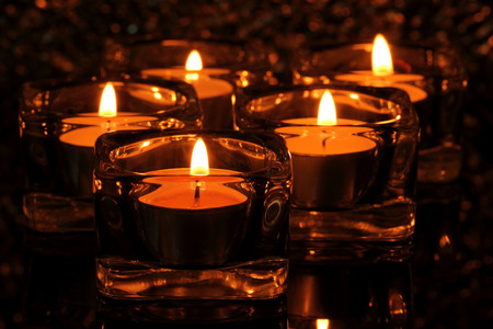 Many candle flames glowing in the dark.