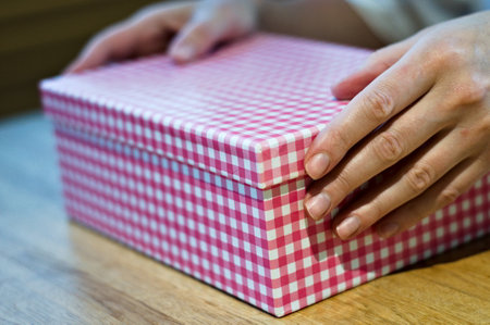 A girl opening a checkered pink box on a wooden table.