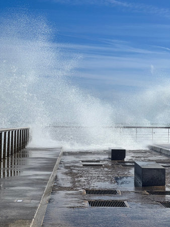 a large wave crashes onto a wet pier with blue sky, copyspace for banner.の写真素材
