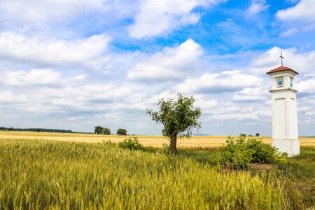 A little Christian Chapel in the middle of Upper Austria rural field with golden yellow grain during a beautiful sunny day under blue skyの写真素材