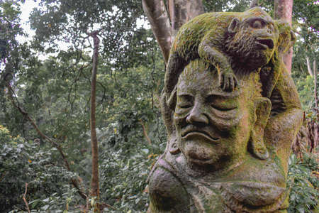 Statue of a monkey sitting on a human head covered by moss in the Sacret Monkey Forest in Ubud Bali...