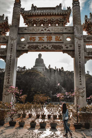 Tourist girl observing the Tian Tan Buddha at the Lantau Island in Hong Kong through traditional Chinese gateのeditorial素材