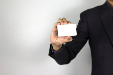 A smart Man holding mock-up white card on white background, a business man wearing dark suit and his hand holding white cardの写真素材