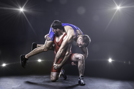 Two freestyle wrestlers in red and blue uniform wrestling against the lights on background Two freestyle wrestlers in red and blue uniform wrestling against the lights on background