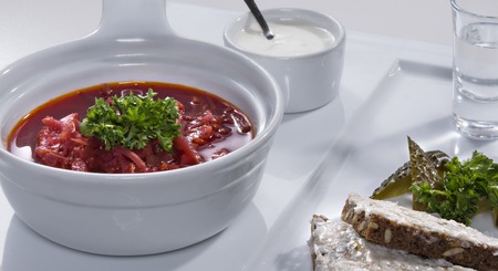 Ukrainian national red borscht soup served with a sour cream, salo sandwich and salty cucumbers decorated with parsley on white plateの写真素材