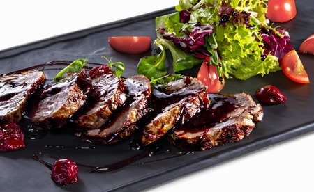 Roasted slices of veal seasoned with cherry sauce and salad on white tableの写真素材