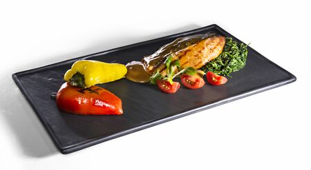 Fried salmon steak with green spinach, grilled pepper decorated with fresh tomatoes isolated on whiteの写真素材