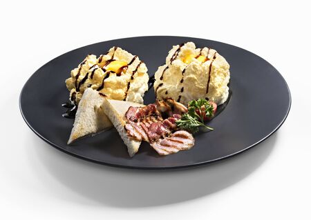 Eggs in clouds with fried bacon and toasts on black plateの写真素材